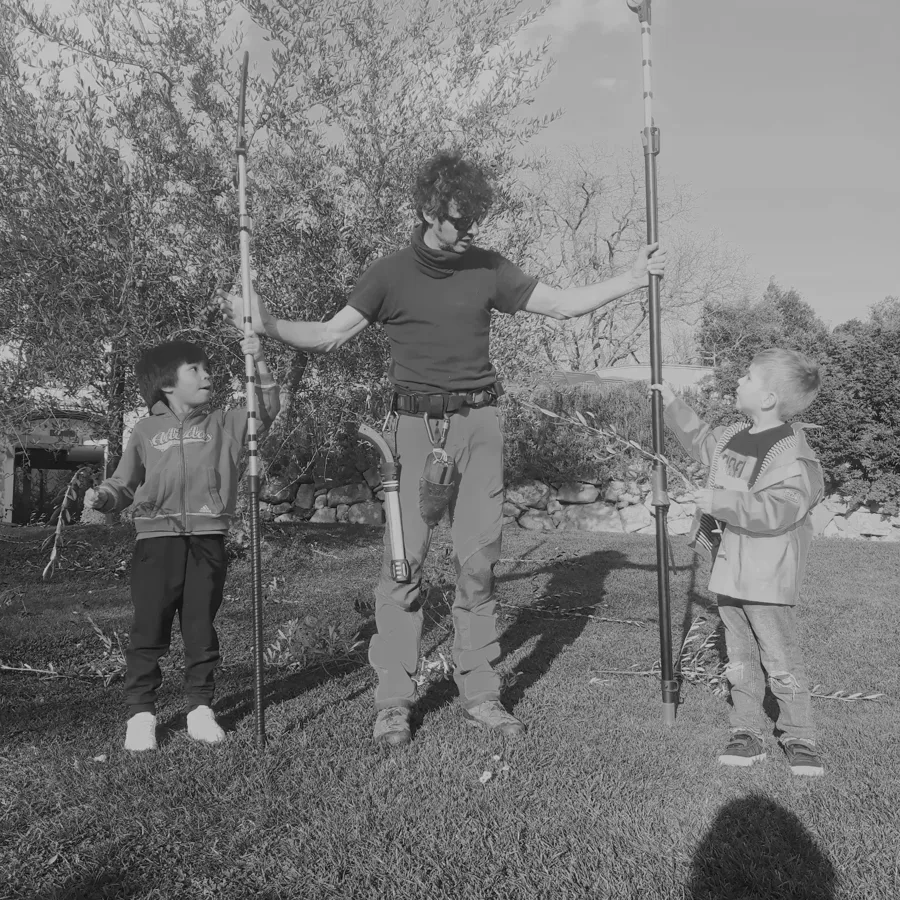 Un arboricoltore con due bambini che reggono aste da potatura in un uliveto